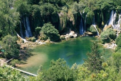 Kravice waterfalls seen from an aerial view surrounded by thick forests with a pool of water in the center.