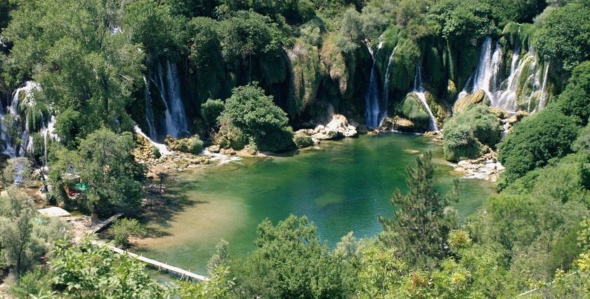 Kravice waterfalls seen from an aerial view surrounded by thick forests with a pool of water in the center.