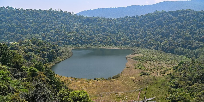 Lake in West Bengal with a small greenish water body, surrounded by green shores and green mountains.