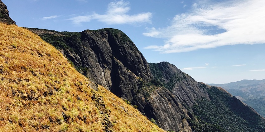 An image of the Kumara Parvatha Trek, a rugged mountain landscape with grass, steep cliffs and the sky.