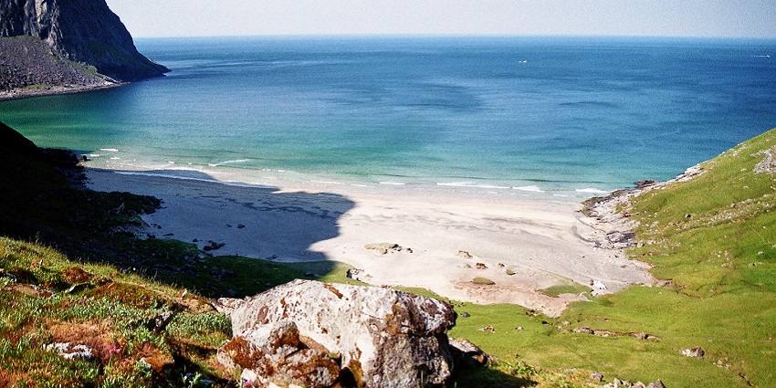 An image of Kvalvika Beach with clear blue waters and a rugged mountain backdrop.