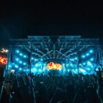 A vibrant nightlife scene at an outdoor music festival, with a massive illuminated stage