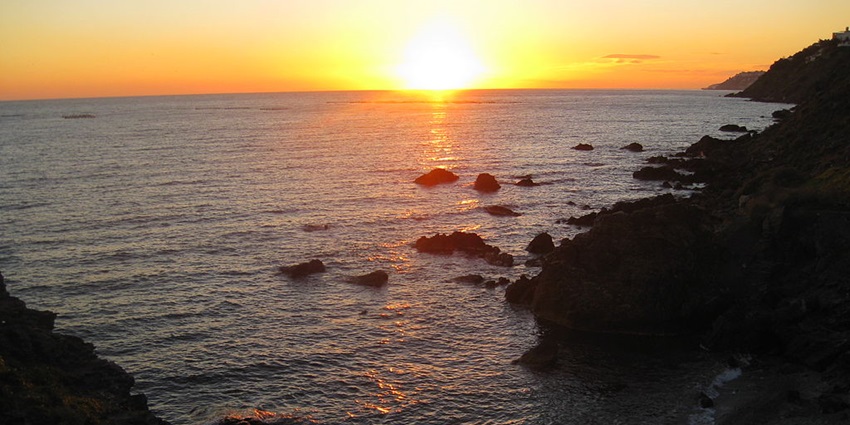 Image of La Caleta Beach during sunset with golden colour sky and sunset reflection water