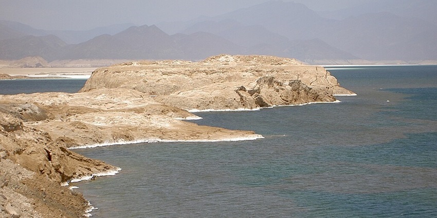 An image view of Lake Assal in Africa with turquoise waters, salt flats, and a rugged landscape