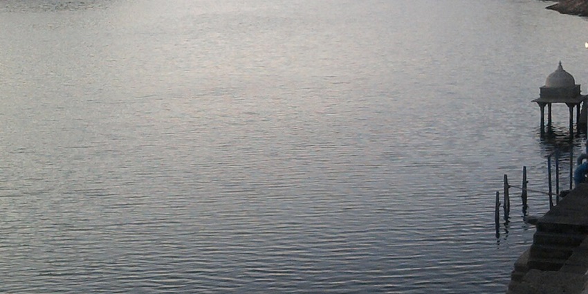 A peaceful view of Lake Badi during sunrise in Udaipur surrounded by green hills and trees