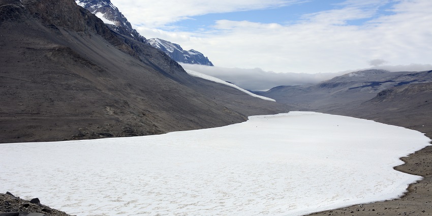 Frozen Lake Bonney in Antarctica, surrounded by sandy mountains with snowy peaks