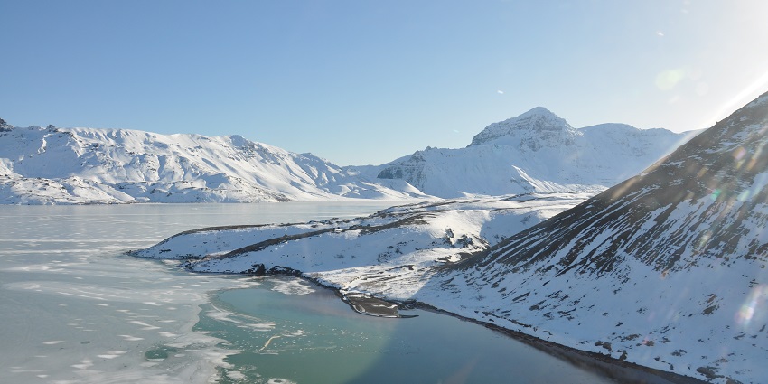 Frozen lake with sunlight falling on the lake and snow-covered ice slopes on the side