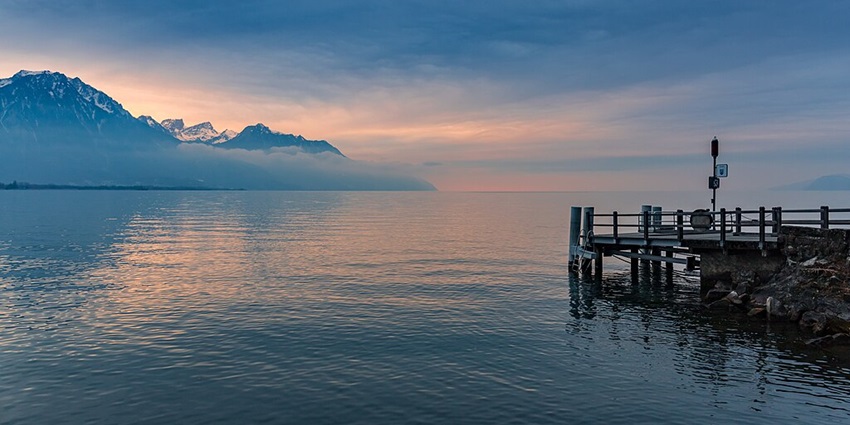 An image view of Geneva Lake in Switzerland with clear waters, surrounding mountains, and Chillon Castle