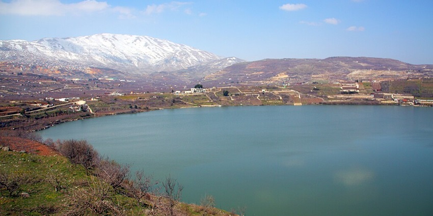 A scenic view of the Ram Lake in Israel, surrounded by snowy mountains and greenery.