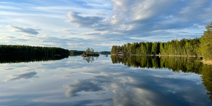 An Image of Lake Saimaa surrounded by dense forests under a partly cloudy sky.
