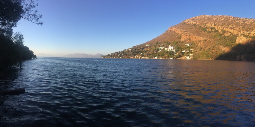 A panoramic view of a lake in South Africa with trees on one side and mountains on the other