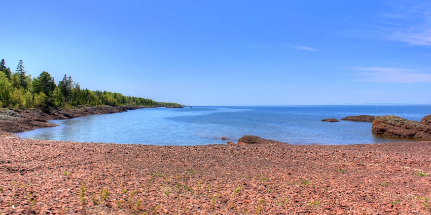 An image of Lake Superior with tropical green waters, surrounded by a scenic and rugged shoreline.