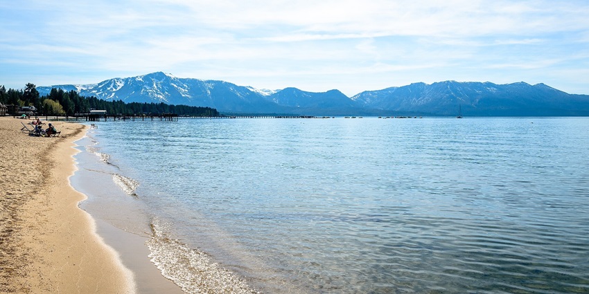 An image of Lake Tahoe with sandy shoreline, people on beachside chairs and distant trees