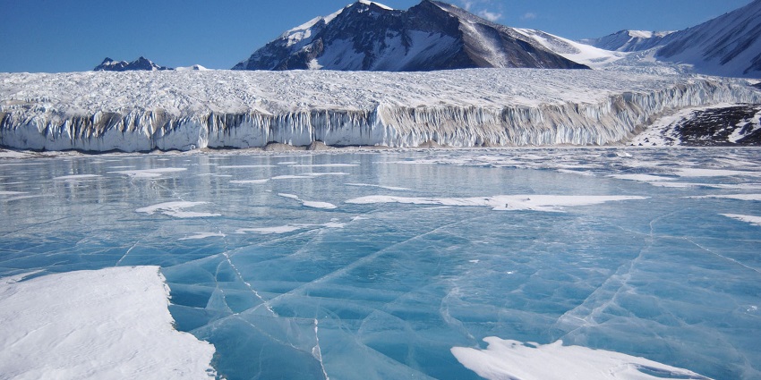 Frozen lake in Antarctica with thick ice and snow-covered mountains in the background