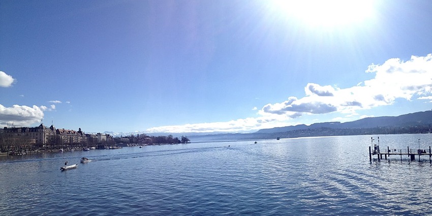 An image view of Zurich Lake in Switzerland with calm waters, boats, and a cityscape in the background