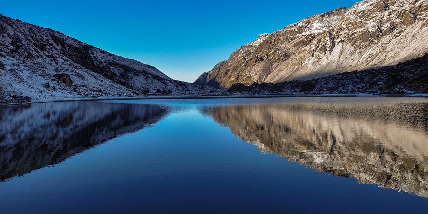 Samiti Lake with hills covered in snow and their reflection on the clear glass lake.