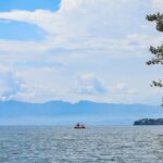 An image view of Kivu Lake in Rwanda with fishermen rowing a boat, calm waters, and a backdrop