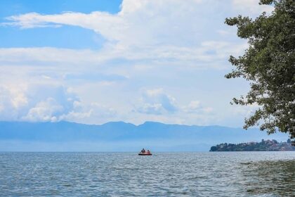 An image view of Kivu Lake in Rwanda with fishermen rowing a boat, calm waters, and a backdrop