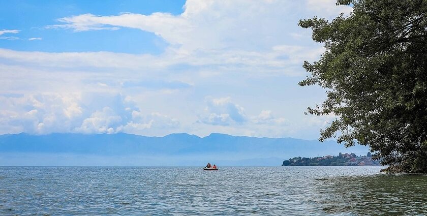 An image view of Kivu Lake in Rwanda with fishermen rowing a boat, calm waters, and a backdrop