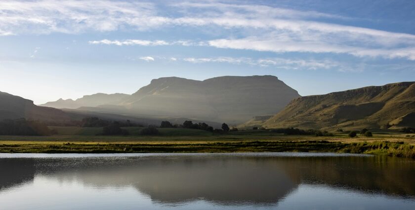 A lake near a mountain under a blue sky with the mountain shadow seen in the waters