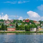 The gentle water of Mirik Lake with many houses and buildings beyond the shore in greenery.