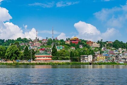 The gentle water of Mirik Lake with many houses and buildings beyond the shore in greenery.