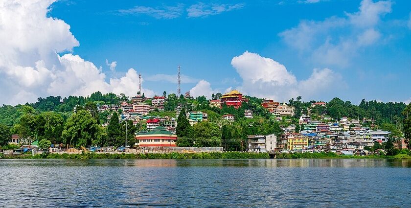 The gentle water of Mirik Lake with many houses and buildings beyond the shore in greenery.