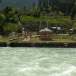 An image of Pahalgam lakefront viewpoint with vehicles and people sitting in a shed