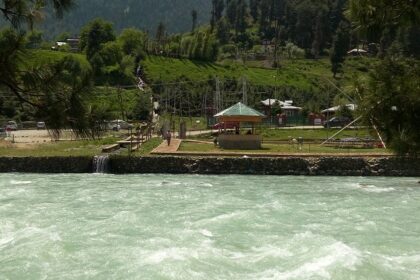 An image of Pahalgam lakefront viewpoint with vehicles and people sitting in a shed