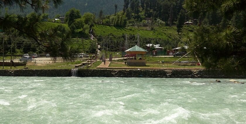 An image of Pahalgam lakefront viewpoint with vehicles and people sitting in a shed