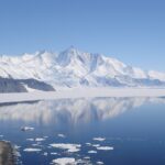 Lake in Antarctica surrounded by white snow and snowy mountains in the background