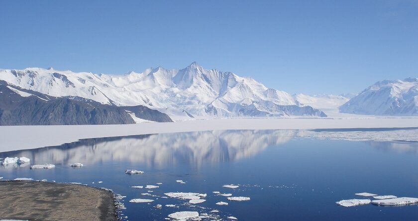 Lake in Antarctica surrounded by white snow and snowy mountains in the background