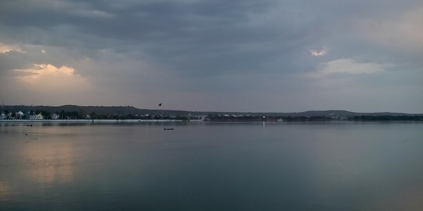 An image of Lakha Banjara Lake Sagar with bird flying, a distant boat and small mountains