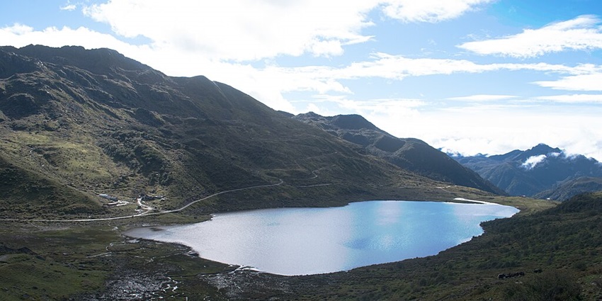 Lake with bright blue water, a trekking trail on the hill and surrounded by mountains.