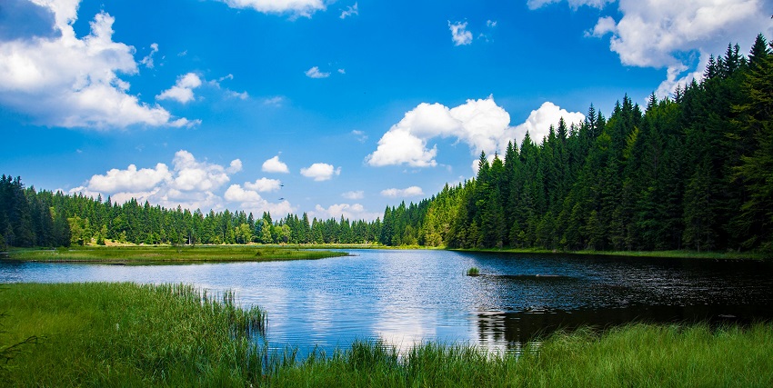 Lake surrounded by green grass, hills and mountains partially covered in snow patches