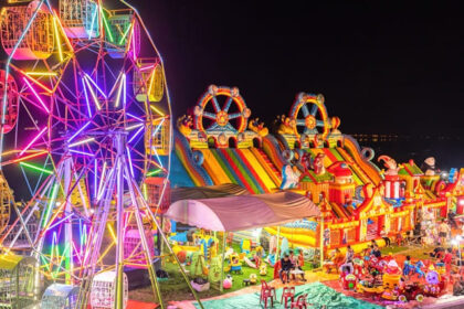 Illuminated Ferris wheel, bouncing castle and carousel in a funfair - Laos nightlife