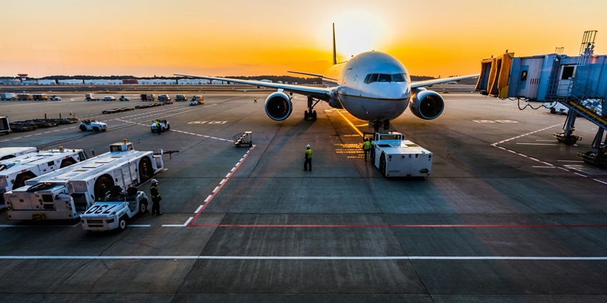 A shot of a plane taking off, with the sun behind and airport infrastructure visible.