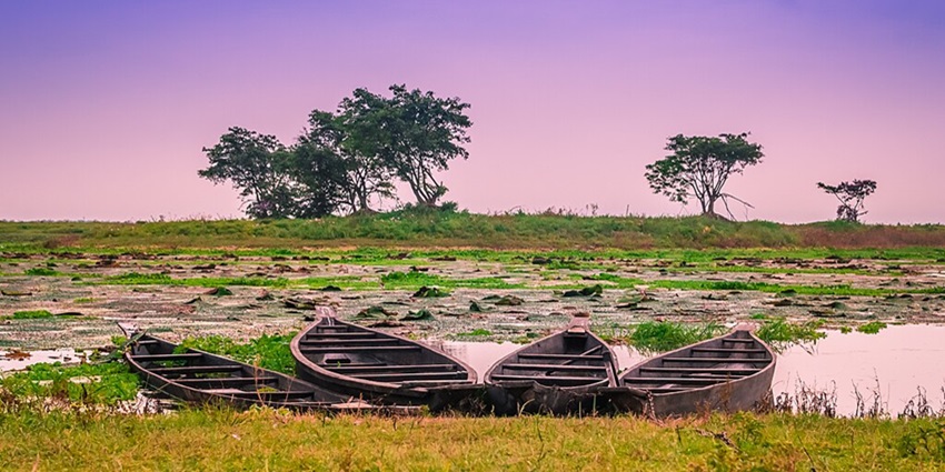 A peaceful lake in Guwahati surrounded by hills and dense vegetation.