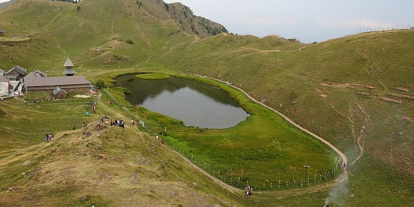 Prashar Lake in summer from the top, surrounded by green shorelines and mountains with people.