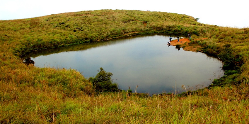 A shot of the Heart Shaped Lake in Kerala, surrounded by verdant hills under blue sky