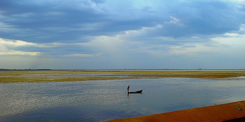 A serene view of the Veeranam Lake, featuring a lone boatman navigating the calm waters