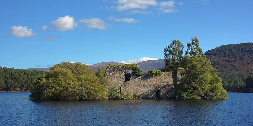 An image of serene Lake with Loch an Eilein Castle ruins and forested surroundings.