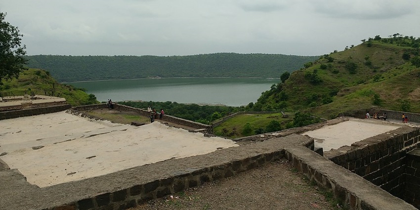 A wide view of Lonar Lake with a group of tourists enjoying near it in the foreground.