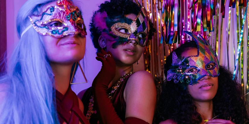 An Image of three elegantly dressed women with masks, celebrating in a New Year party