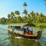 Vembanad Lake with a person in a houseboat and small land with palm trees in the back.