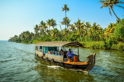 Vembanad Lake with a person in a houseboat and small land with palm trees in the back.