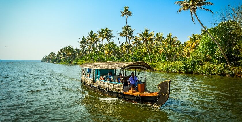 Vembanad Lake with a person in a houseboat and small land with palm trees in the back.