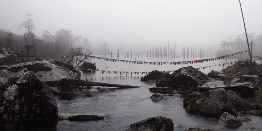 Madhuri Lake on a foggy day, surrounded by stones and decorated with colourful flags.