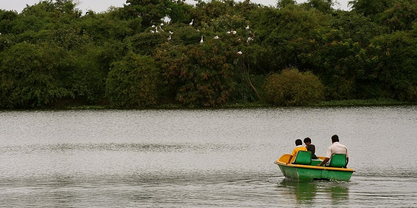 Multiple people boating on a green-yellow boat in Madiwala Lake, one of the famous lakes in Bangalore.