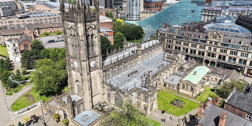 An Image of the aerial view of the Manchester Cathedral, surrounded by building and greenery.
